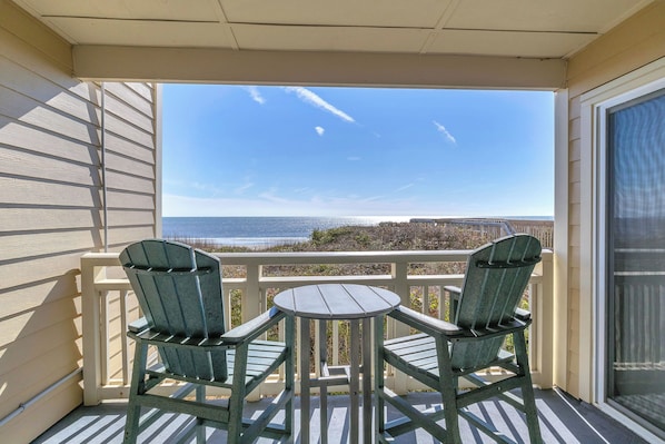 A balcony with two chairs and a small table, overlooking a coastal view. - Sandy Shore: Oceanfront Condo Walking Distance to Golf Course (Caswell Beach)