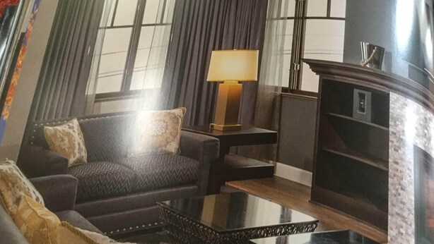 A living room with a dark-colored sofa, a patterned armchair, a glass coffee table, and a side table with a lamp.