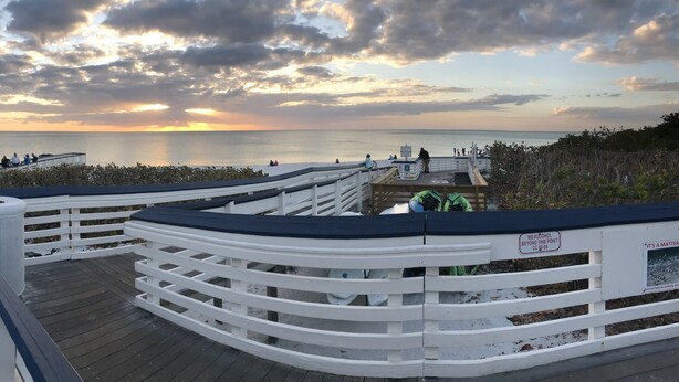 A wooden boardwalk with white railings, leading to a beach area with a thatched-roof structure. - Quiet Studio, minutes from Beaches, Shopping, Dining, 5th Ave and 3rd Street (Naples)