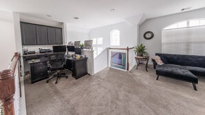 A spacious living area with a dark-colored sofa, a desk with a computer, and a staircase leading to another level. - Beautiful 2 story luxury home in an upscale area! (Houston)