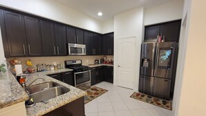 A modern kitchen with dark cabinets, stainless steel appliances, a granite countertop, and a tiled floor. - Beautiful 2 story luxury home in an upscale area! (Houston)