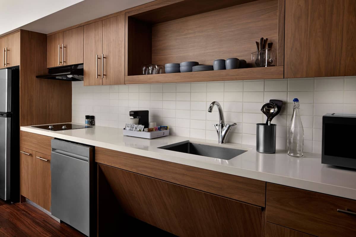 A modern kitchen with wooden cabinets, a stainless steel refrigerator, a double sink, and a coffee machine.