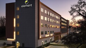 A modern hotel building with a flat facade, multiple windows, and a prominent logo on the side.