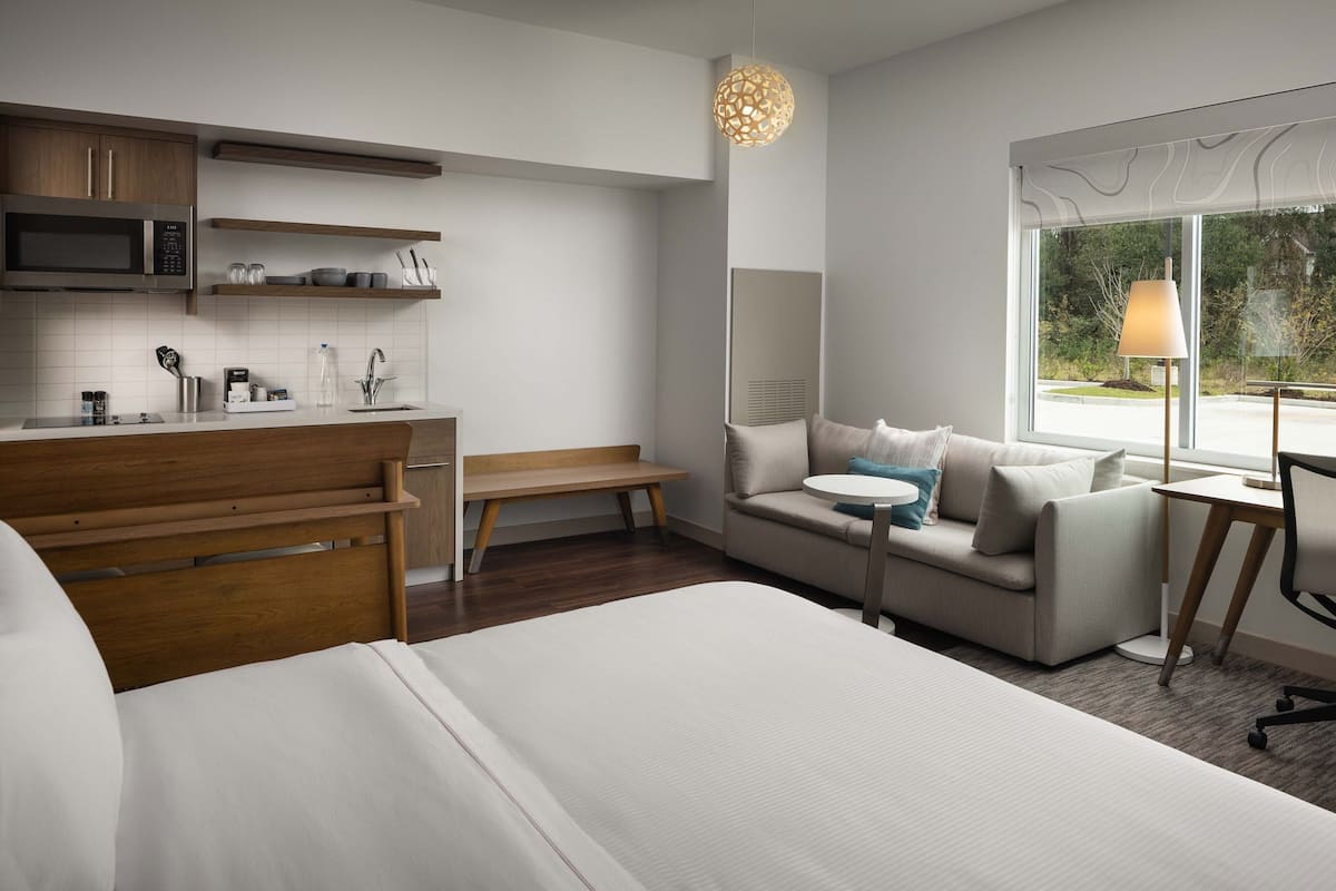 A modern hotel room with a bed, a sofa, a desk, a microwave, and a window with a view.