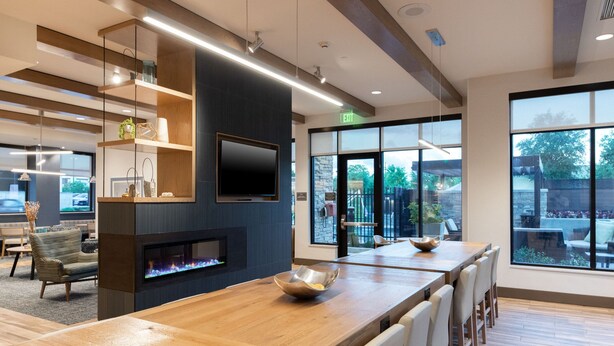Uma sala de jantar moderna com uma longa mesa de madeira, assentos confortáveis, uma televisão de tela plana e uma lareira.