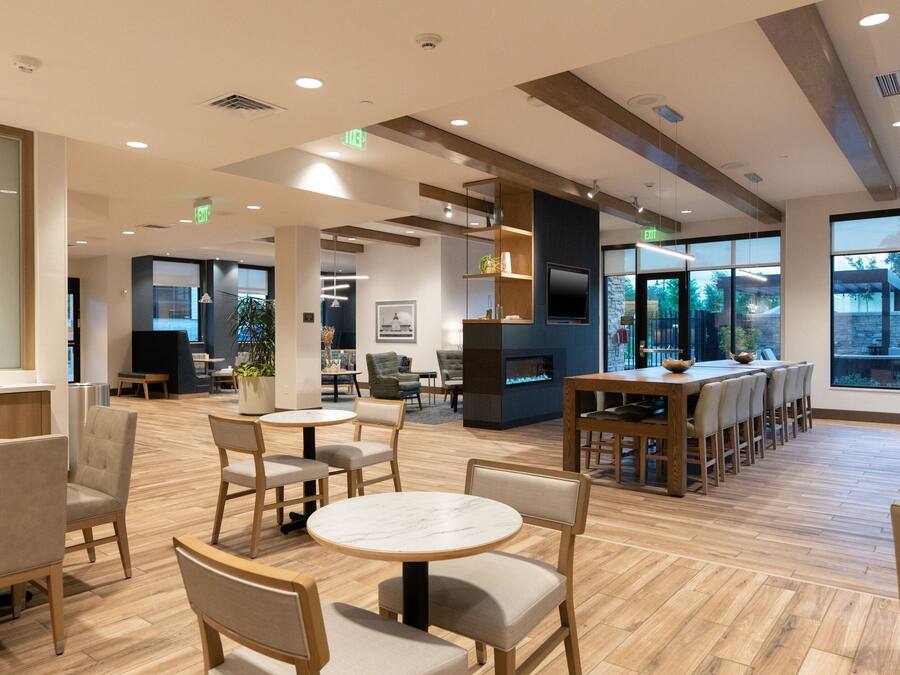 A spacious indoor area with multiple seating arrangements, including round tables and chairs, a long communal table, and a fireplace.