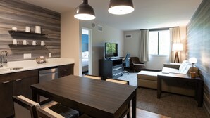 Quarto de hotel moderno com cozinha, mesa de jantar, sofá e TV.