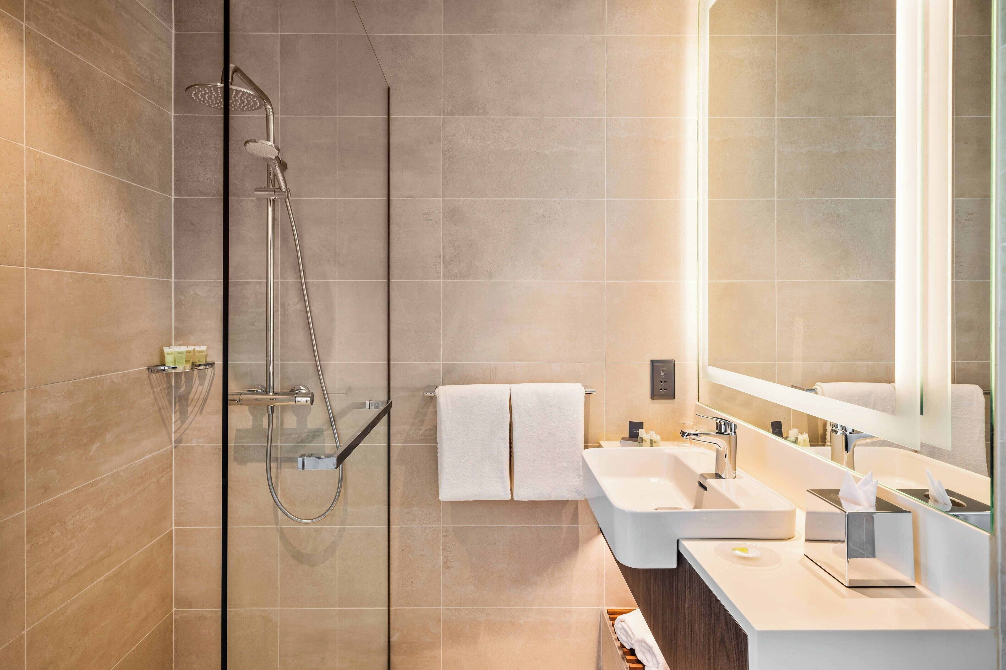 Un baño moderno con ducha de vidrio, dos lavamanos y un espejo grande.