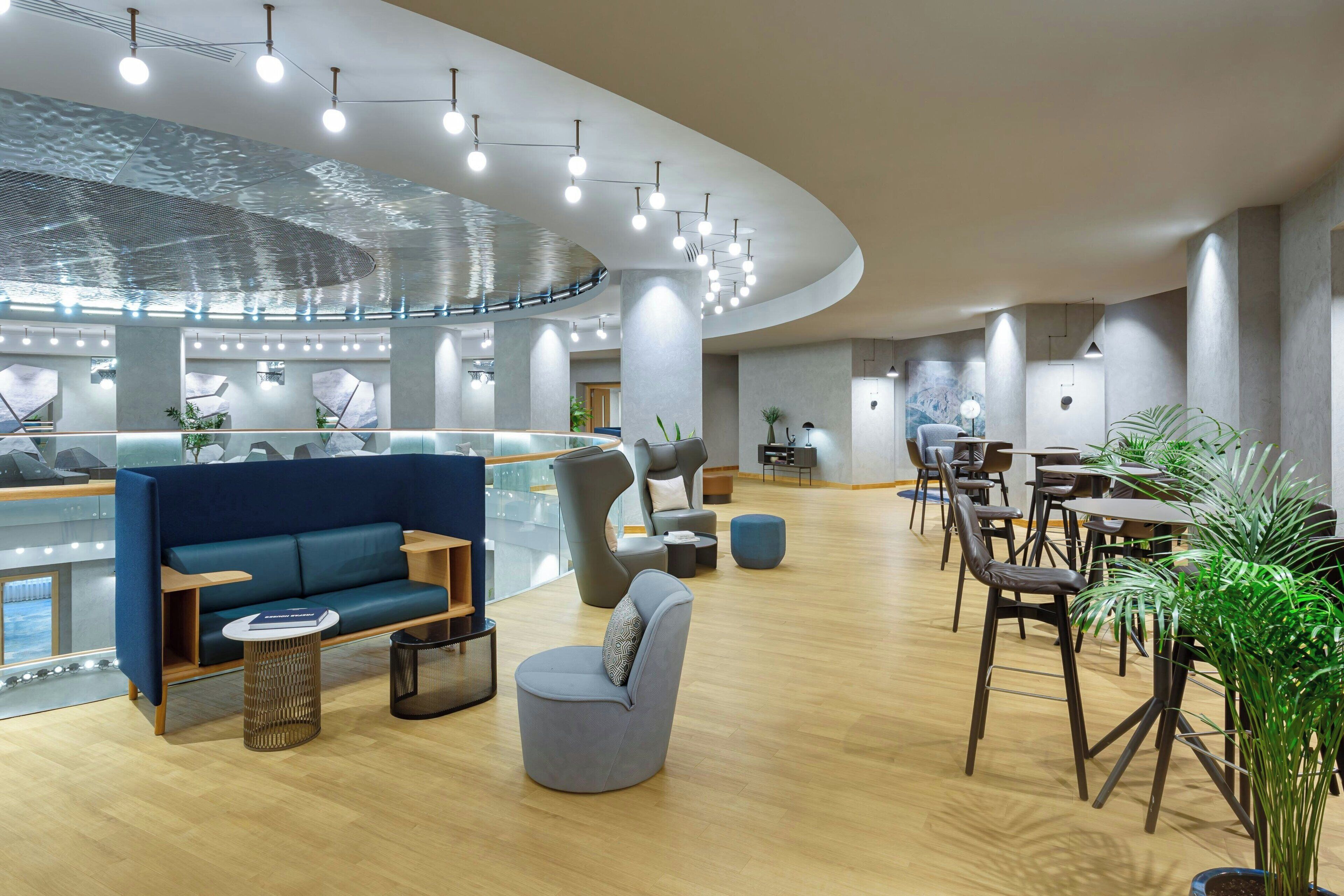 A modern lounge area with seating, a glass railing, and a ceiling with hanging lights.