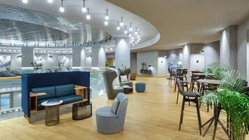 A modern lounge area with seating, a glass railing, and a ceiling with hanging lights.