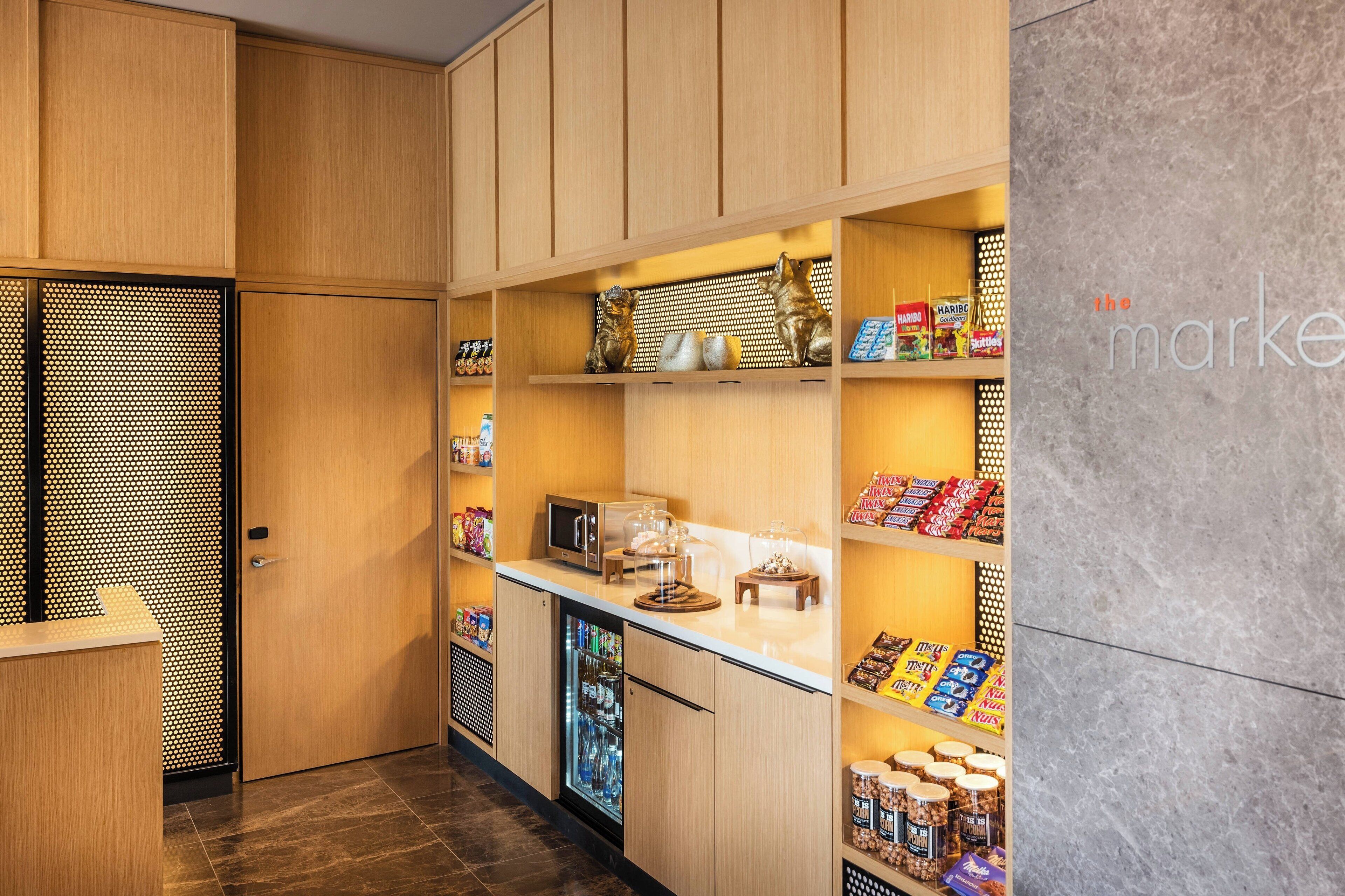 Una kitchenette moderna con armarios de madera, un microondas, un refrigerador y varios aperitivos y condimentos en estantes.