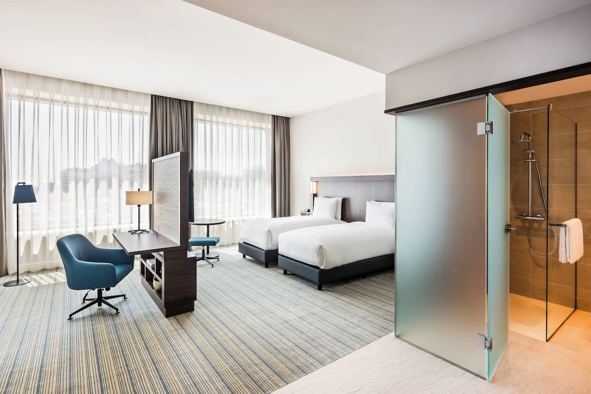 A hotel room with a bed, two bedside tables, a desk, a chair, a TV, and a shower area.