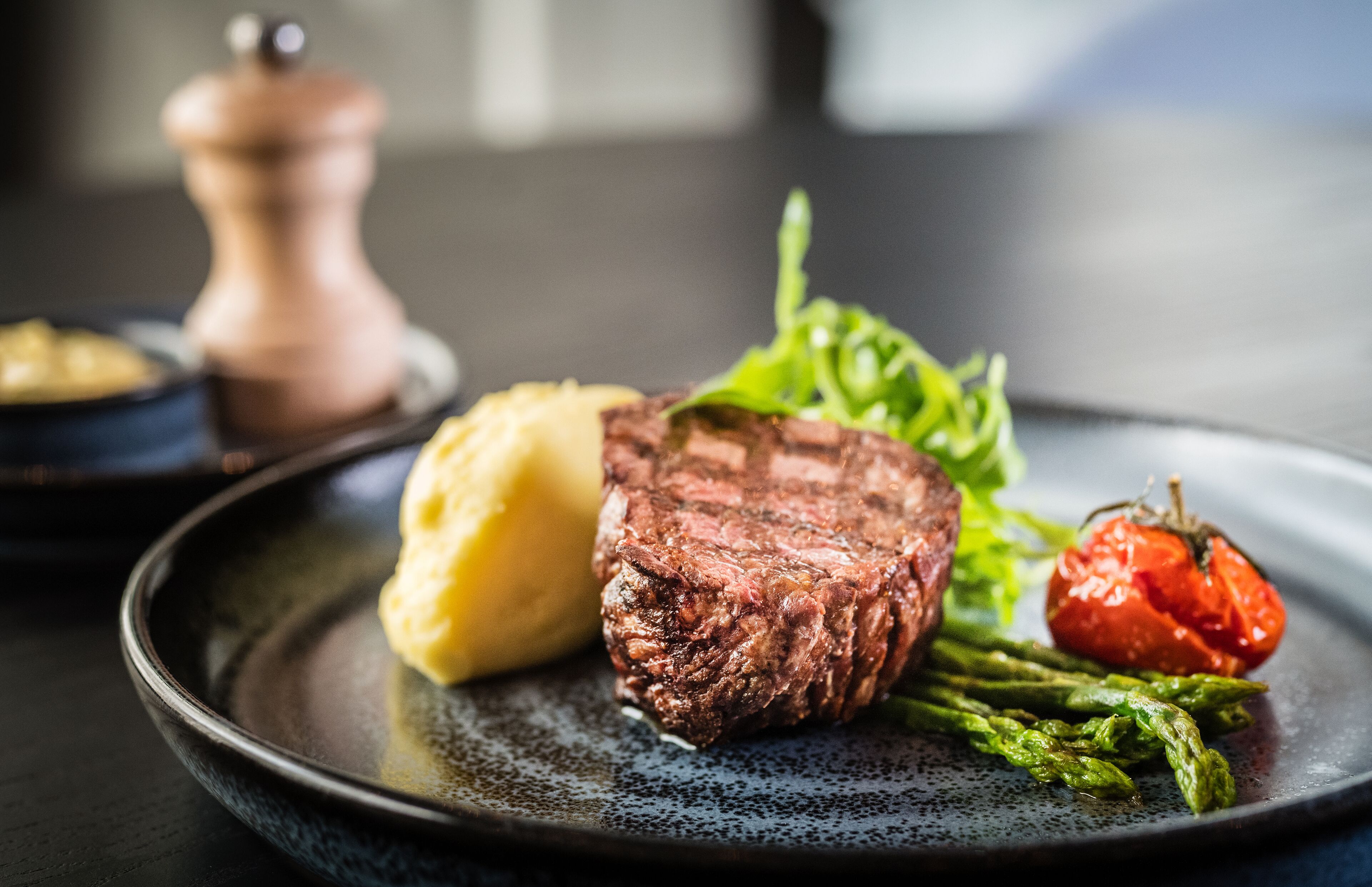 En tallerken med steak, mos kartofler, asparges og en grillet tomat.