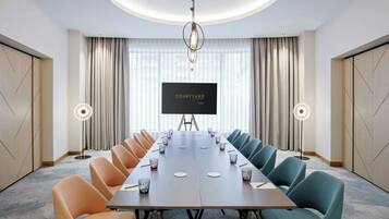 A conference room with a long table, chairs, a projector screen, and a large window with curtains.