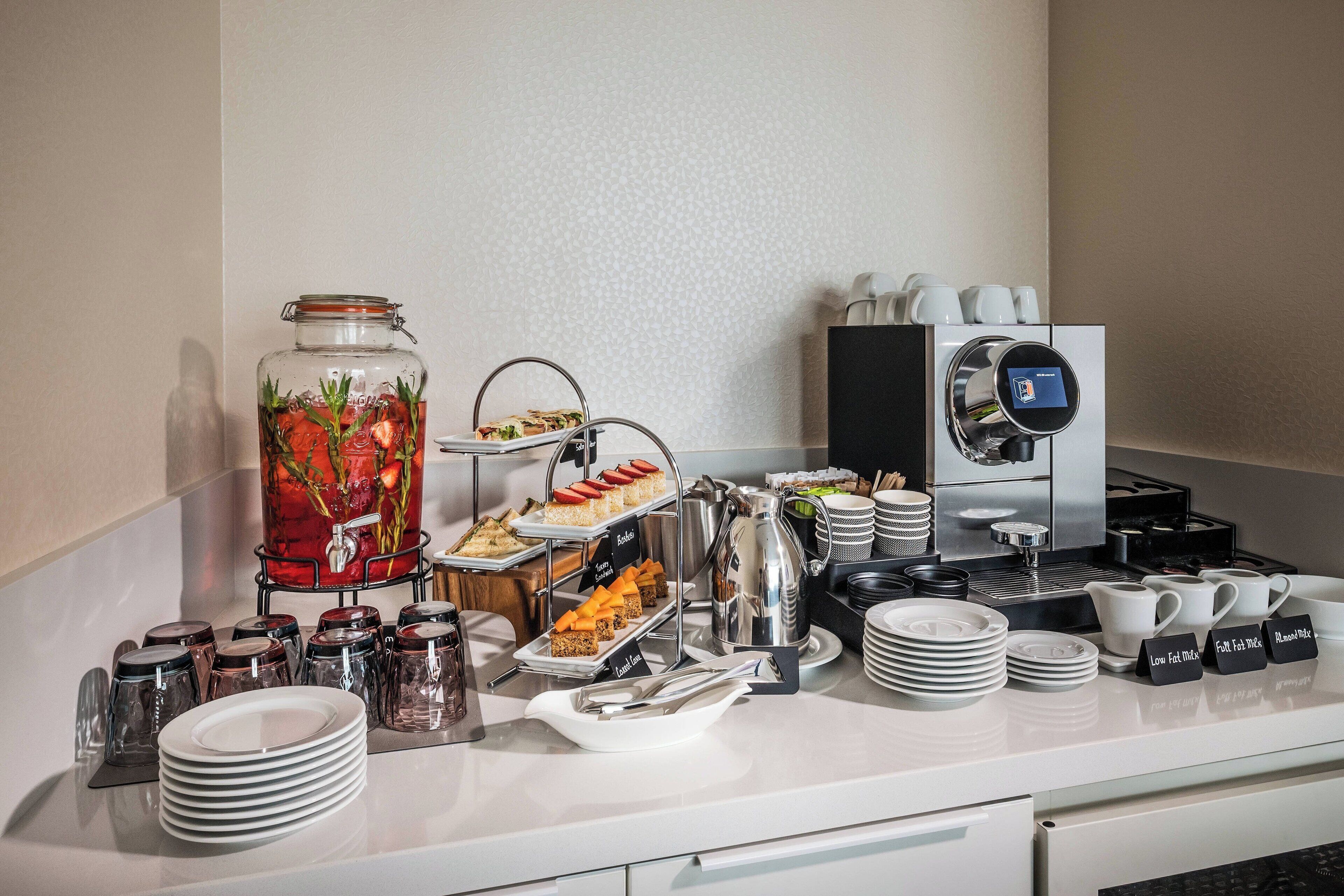 Disposición de un bufé con diversas opciones de comida, una máquina de café y un dispensador de agua.