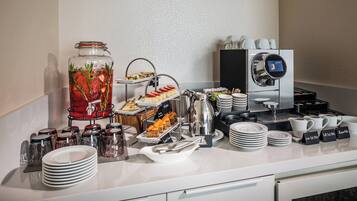 Disposición de un bufé con diversas opciones de comida, una máquina de café y un dispensador de agua.