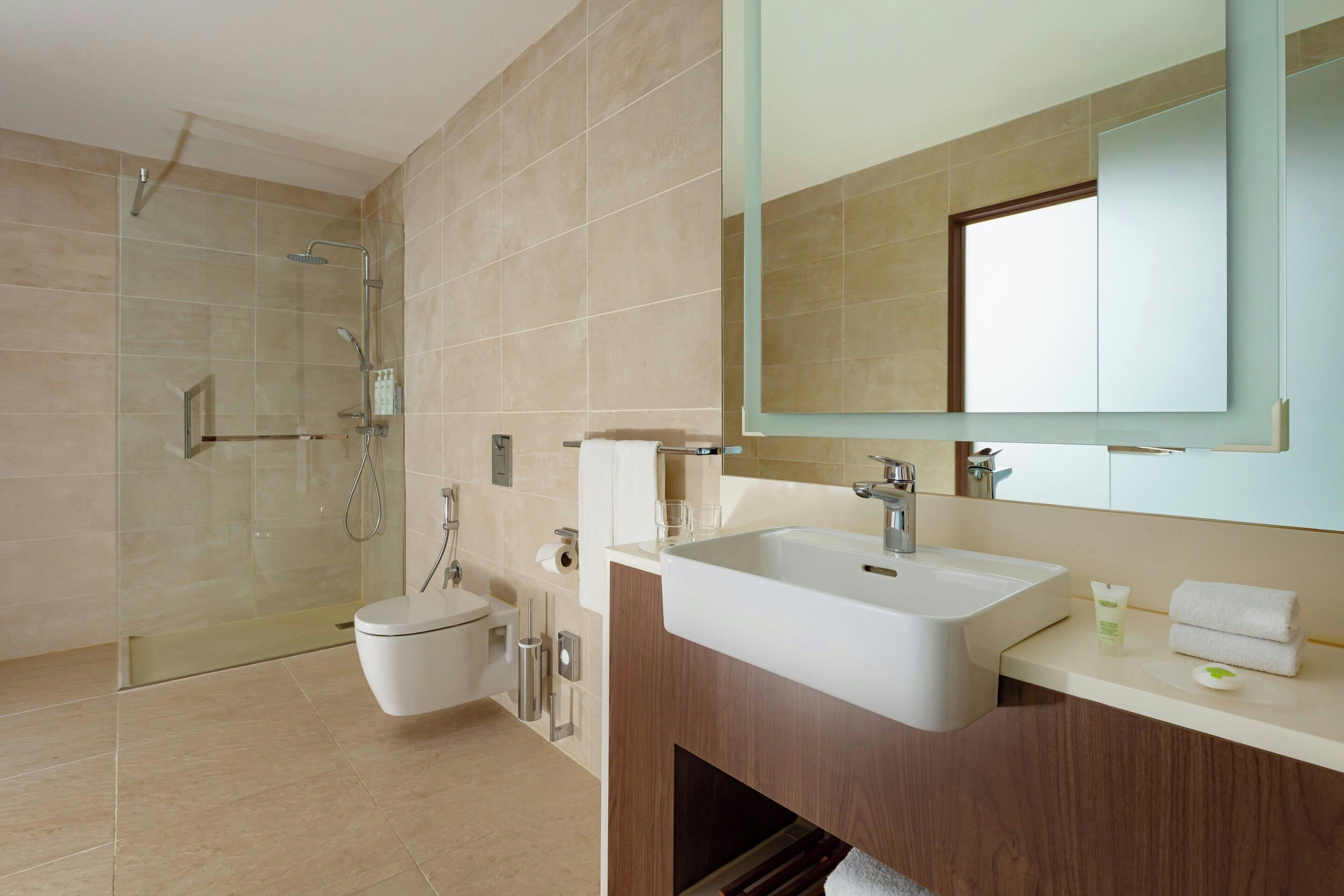 Een moderne badkamer met een douchecabine van glas, een witte wastafel en een grote spiegel.