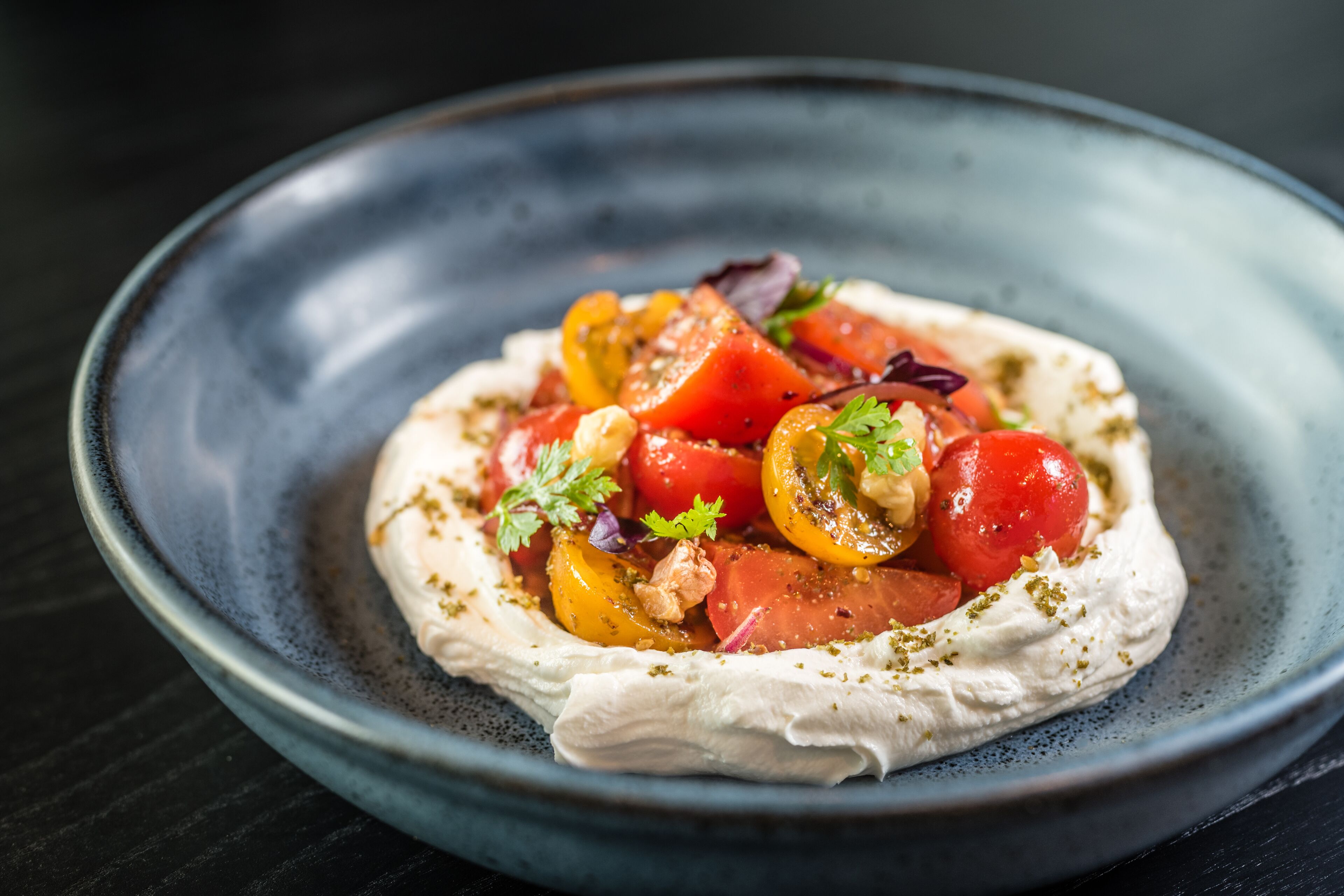 A dish with a creamy base topped with tomatoes and herbs, served on a blue plate.