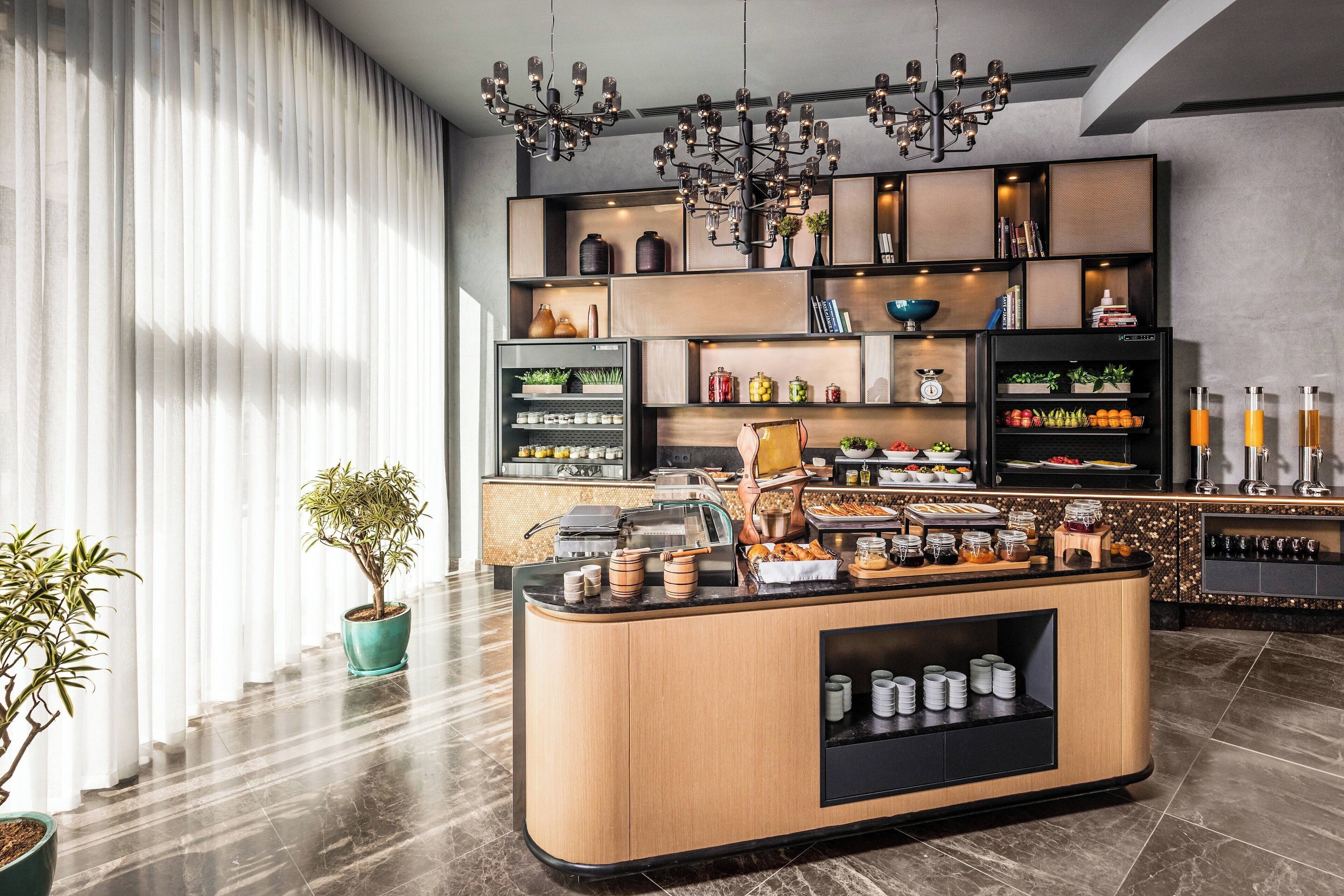 Um hall de hotel moderno com um balcão de café da manhã, plantas em vasos e um lustre.
