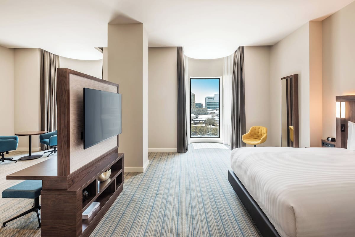A hotel room with a large bed, a TV, a desk, and a view of the city.