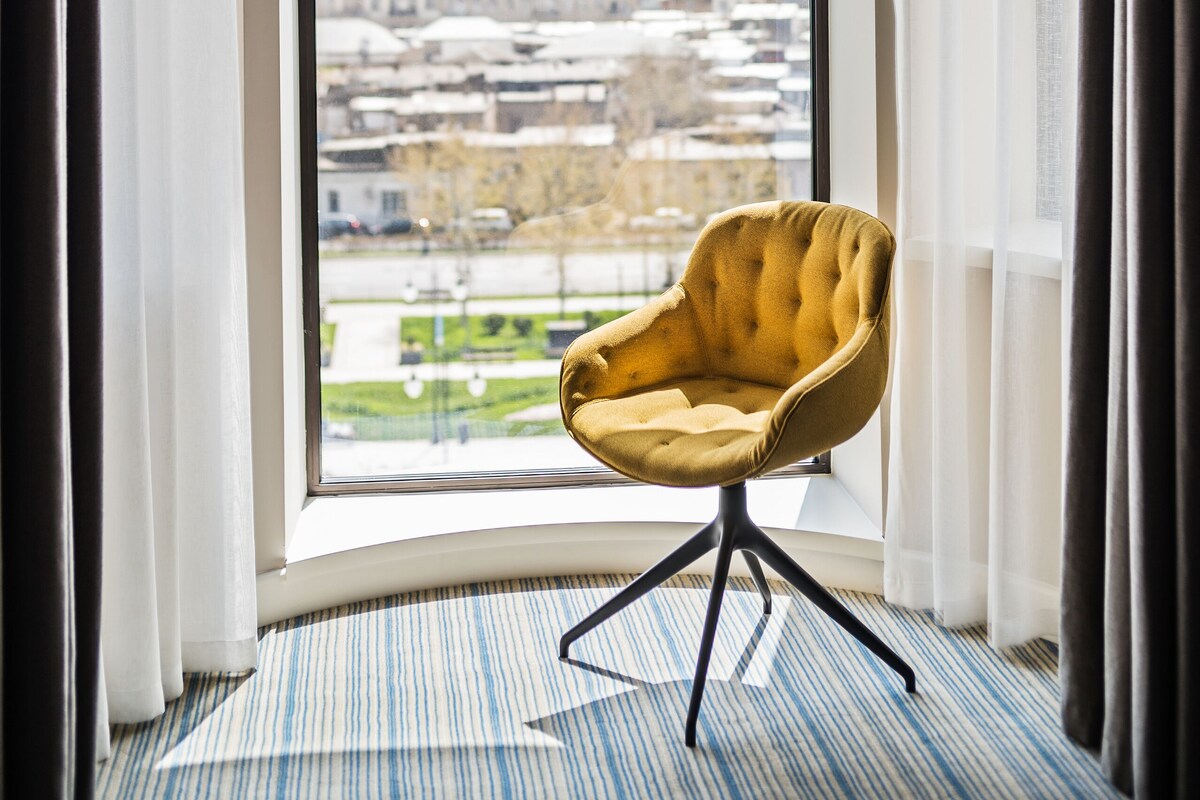 A room with a large window, a yellow chair, and a striped carpet.