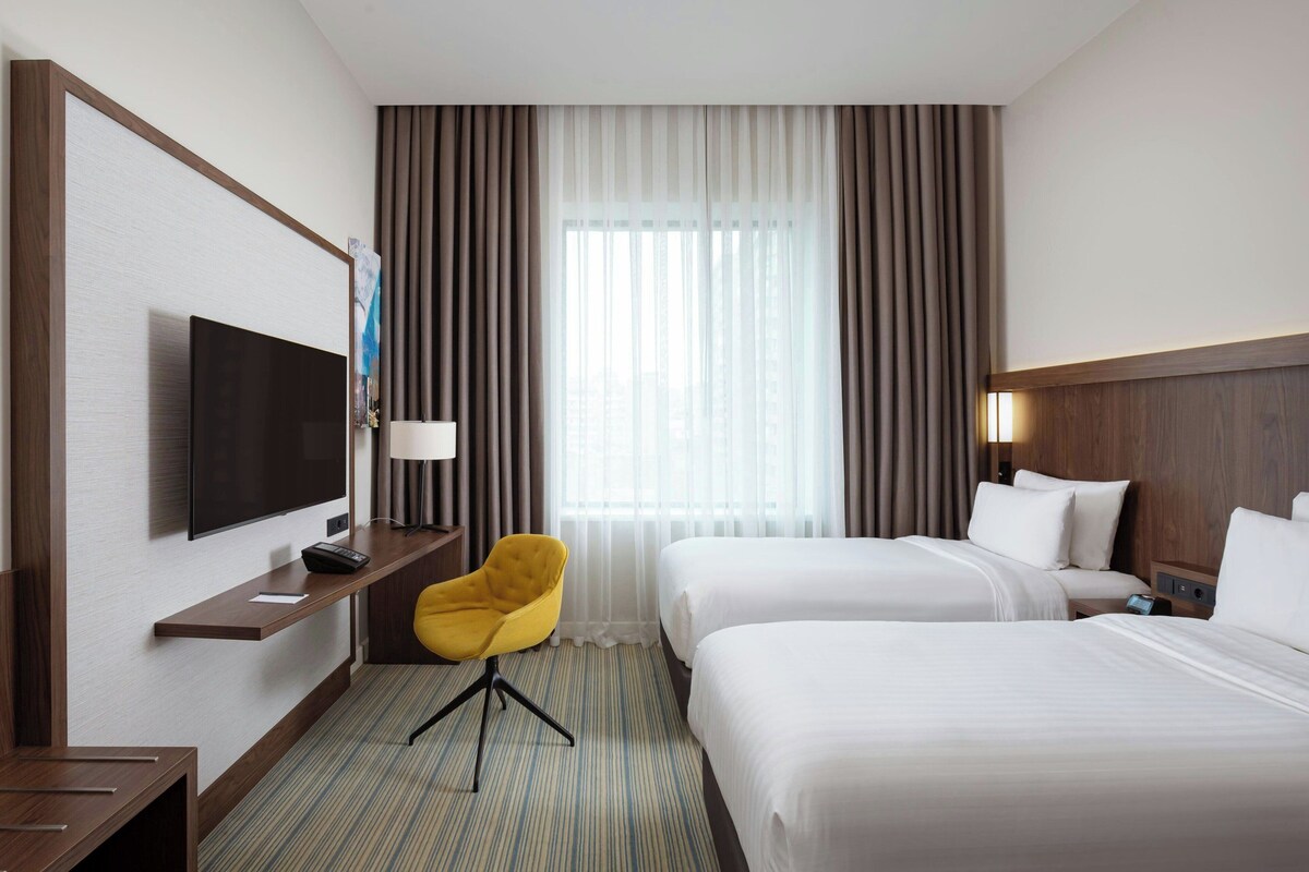 A hotel room with two beds, a TV, a desk, and a chair.