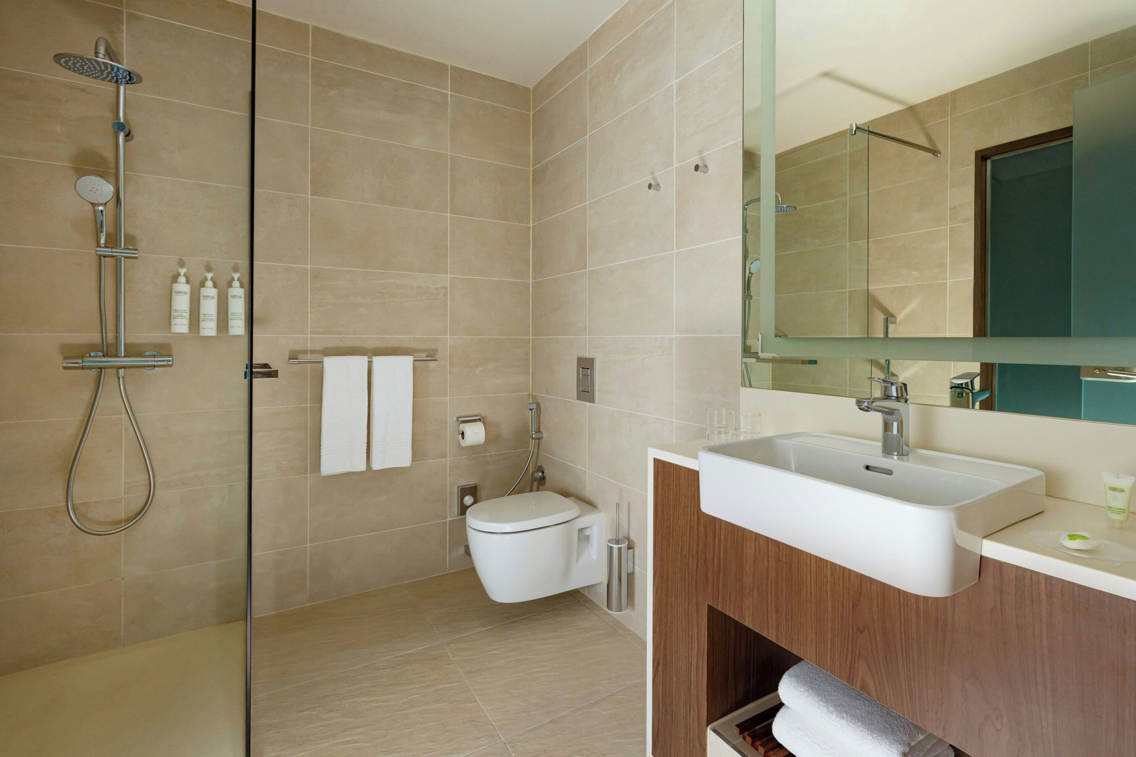 A modern bathroom with a shower, toilet, sink, and a large mirror.