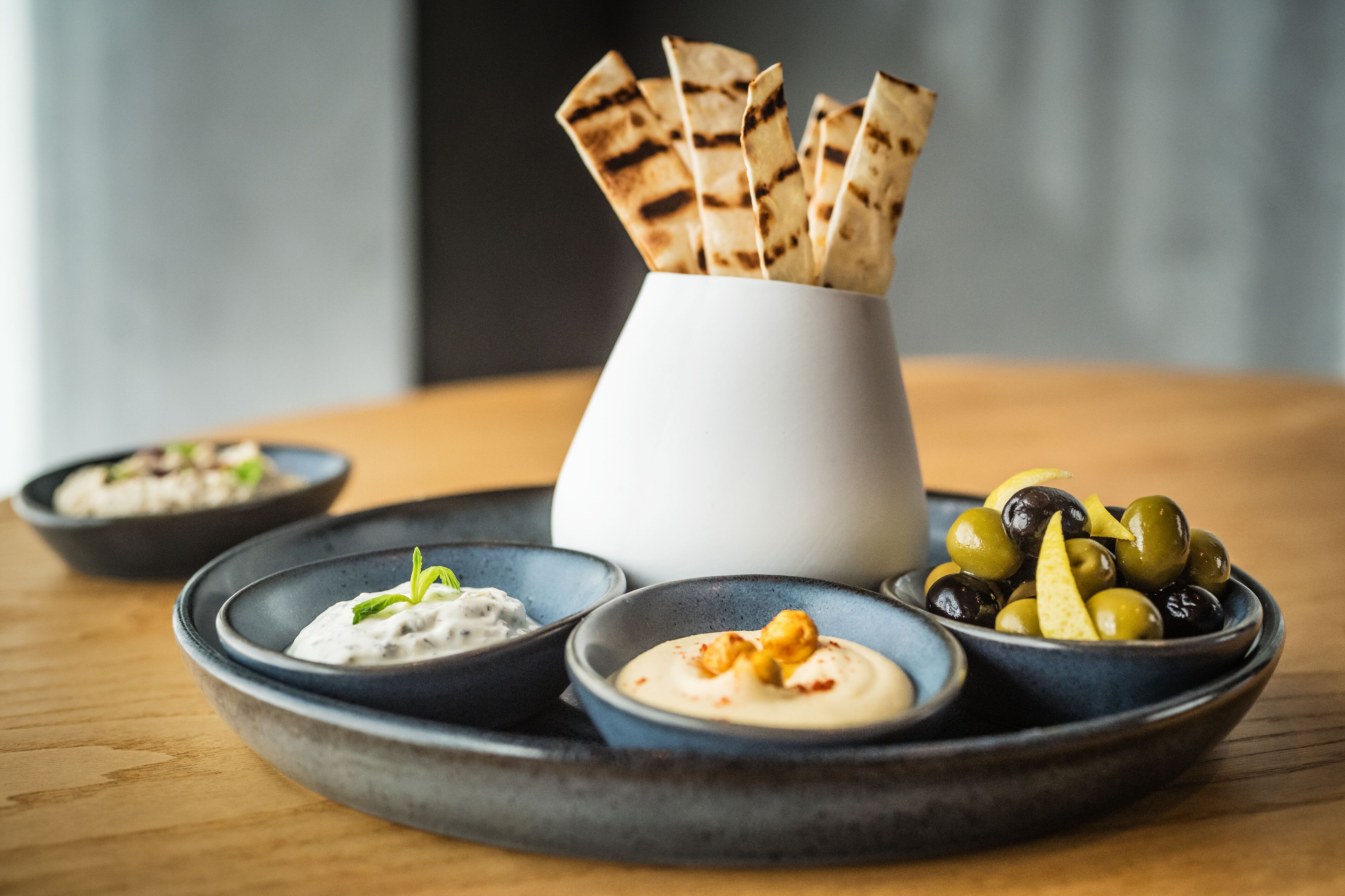A table with three bowls of dips and a bowl of olives.