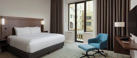Une chambre d’hôtel avec un grand lit, un bureau avec une chaise et une vue sur un immeuble par la fenêtre.