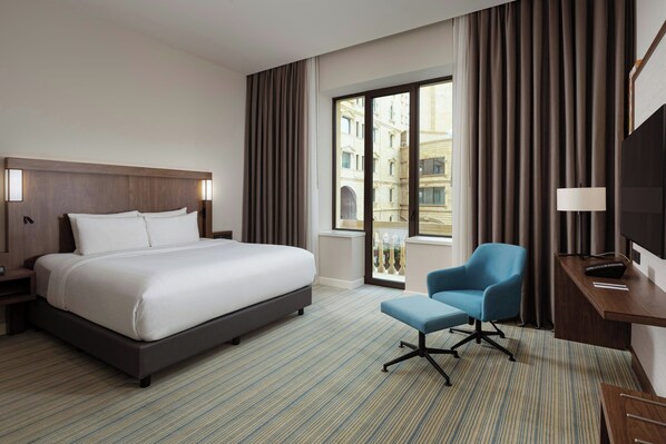 Une chambre d’hôtel avec un grand lit, un bureau avec une chaise et une vue sur un immeuble par la fenêtre.