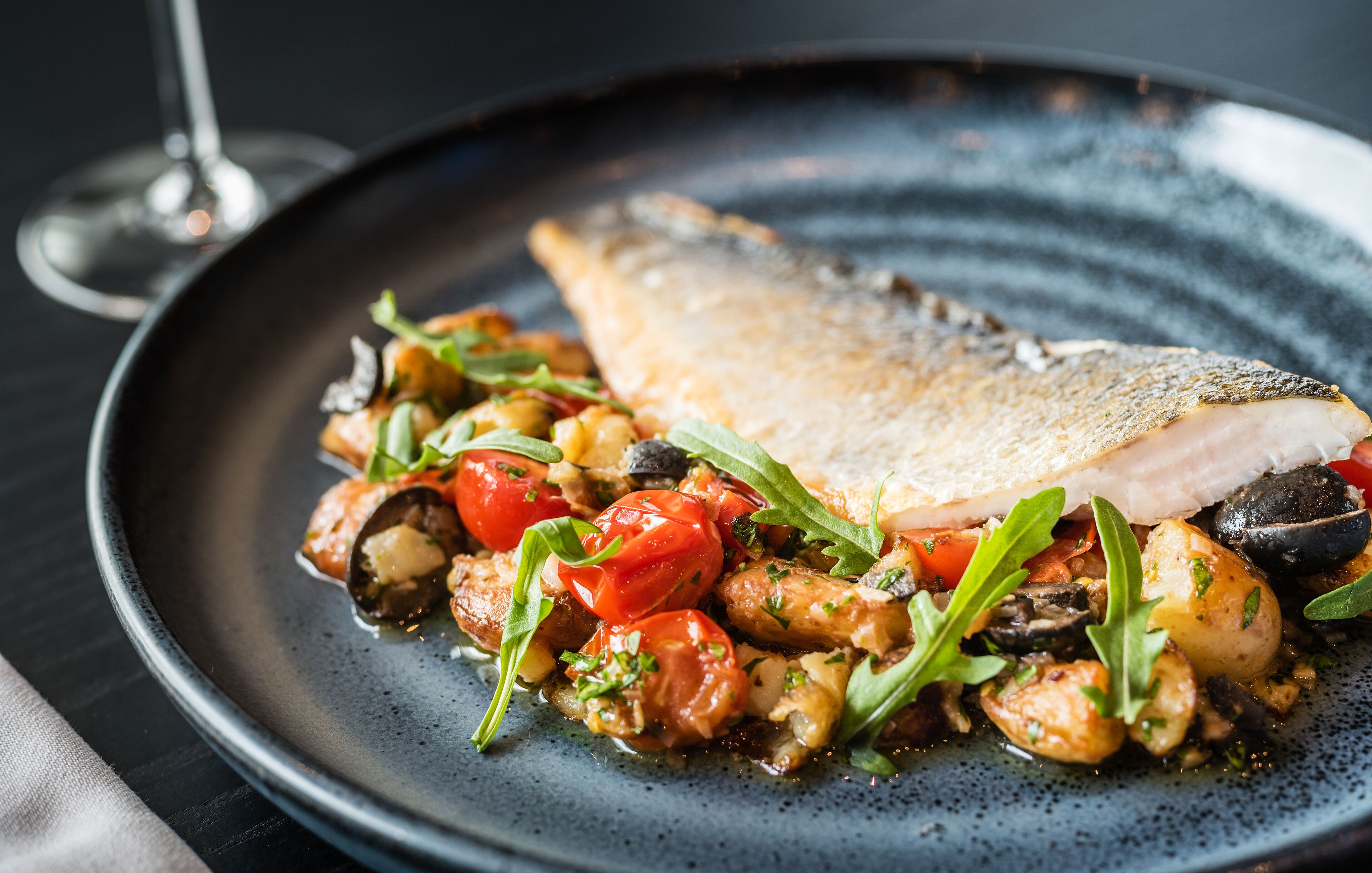 Um prato de comida com filé de peixe, tomates e folhas verdes.