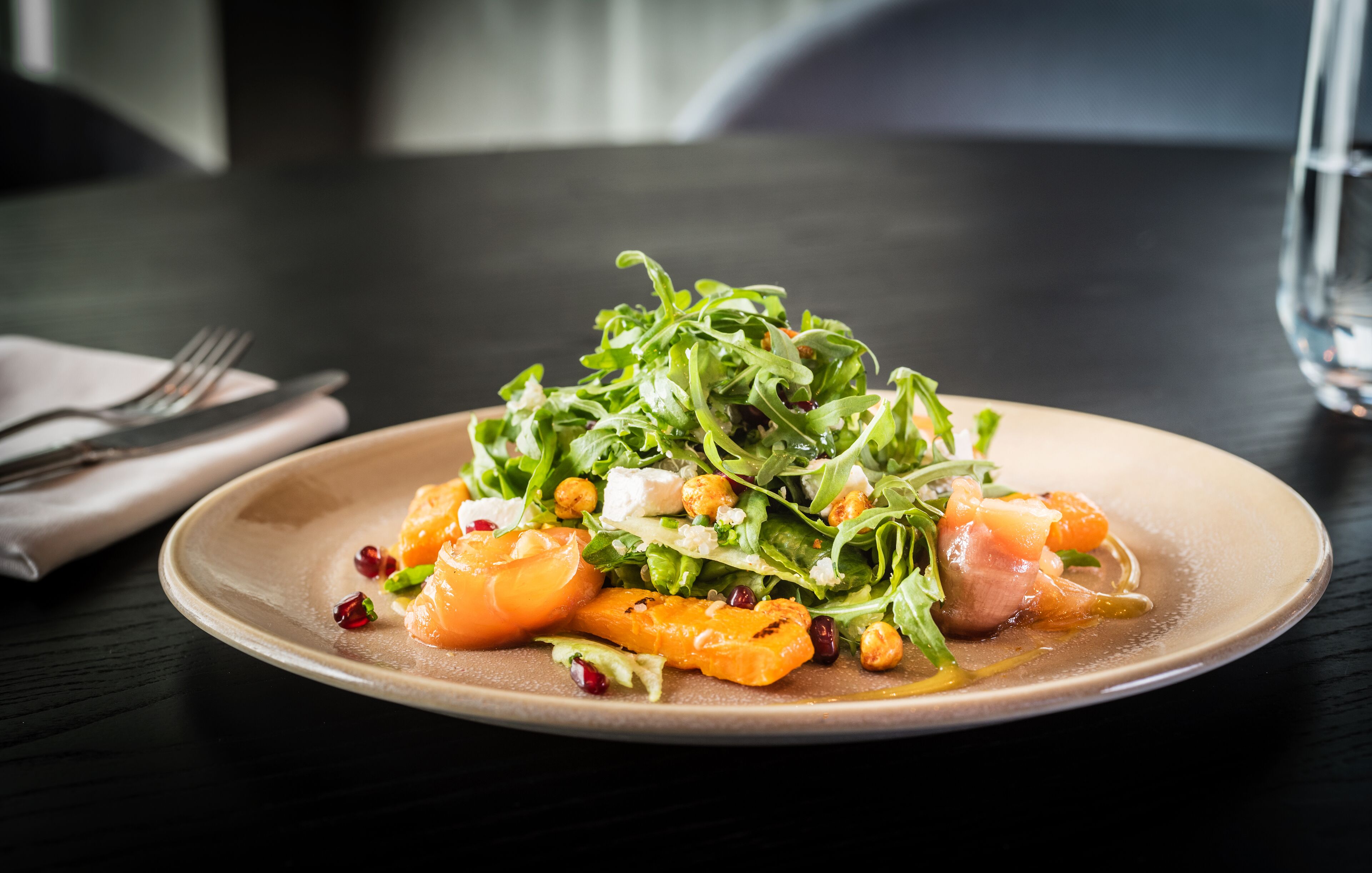 A plate of food with greens, orange slices, and nuts on a table.