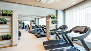 Un gimnasio con varias cintas de correr, equipamiento de ejercicio y plantas en macetas.