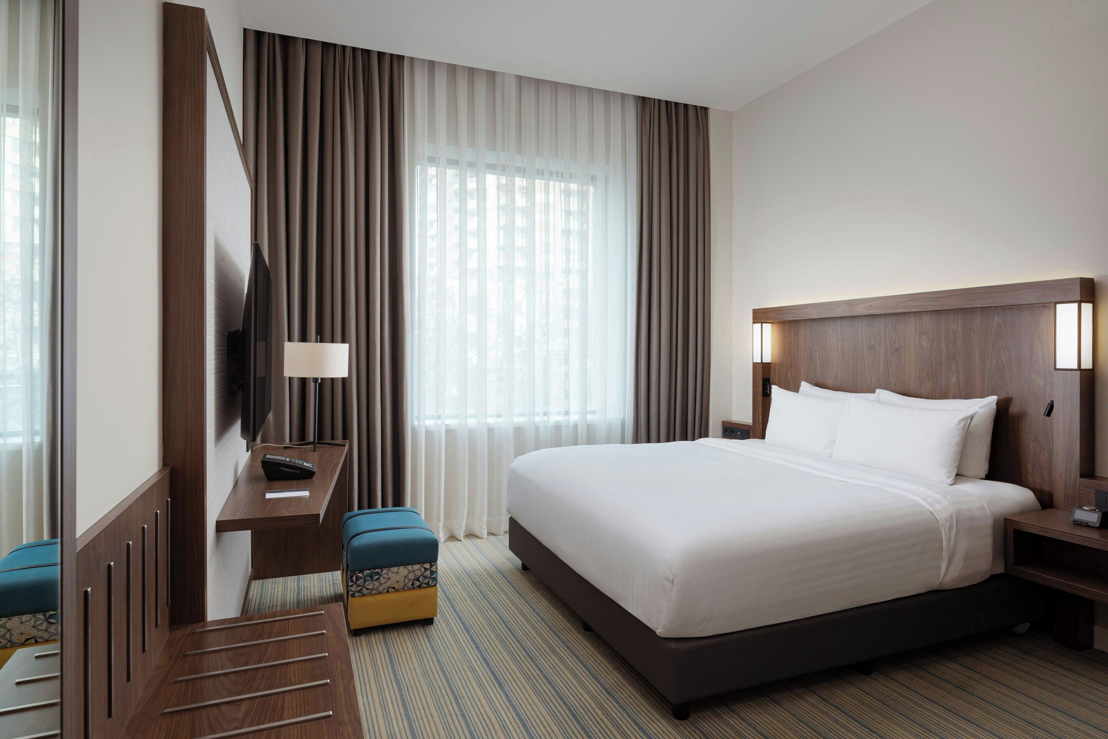 Een hotelkamer met een groot bed, een bureau met lamp, een televisie en een raam met gordijnen.
