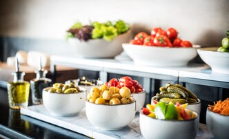 Een buffet tafel met diverse schalen eten, waaronder olijven, kerstomaatjes, augurken en salade.