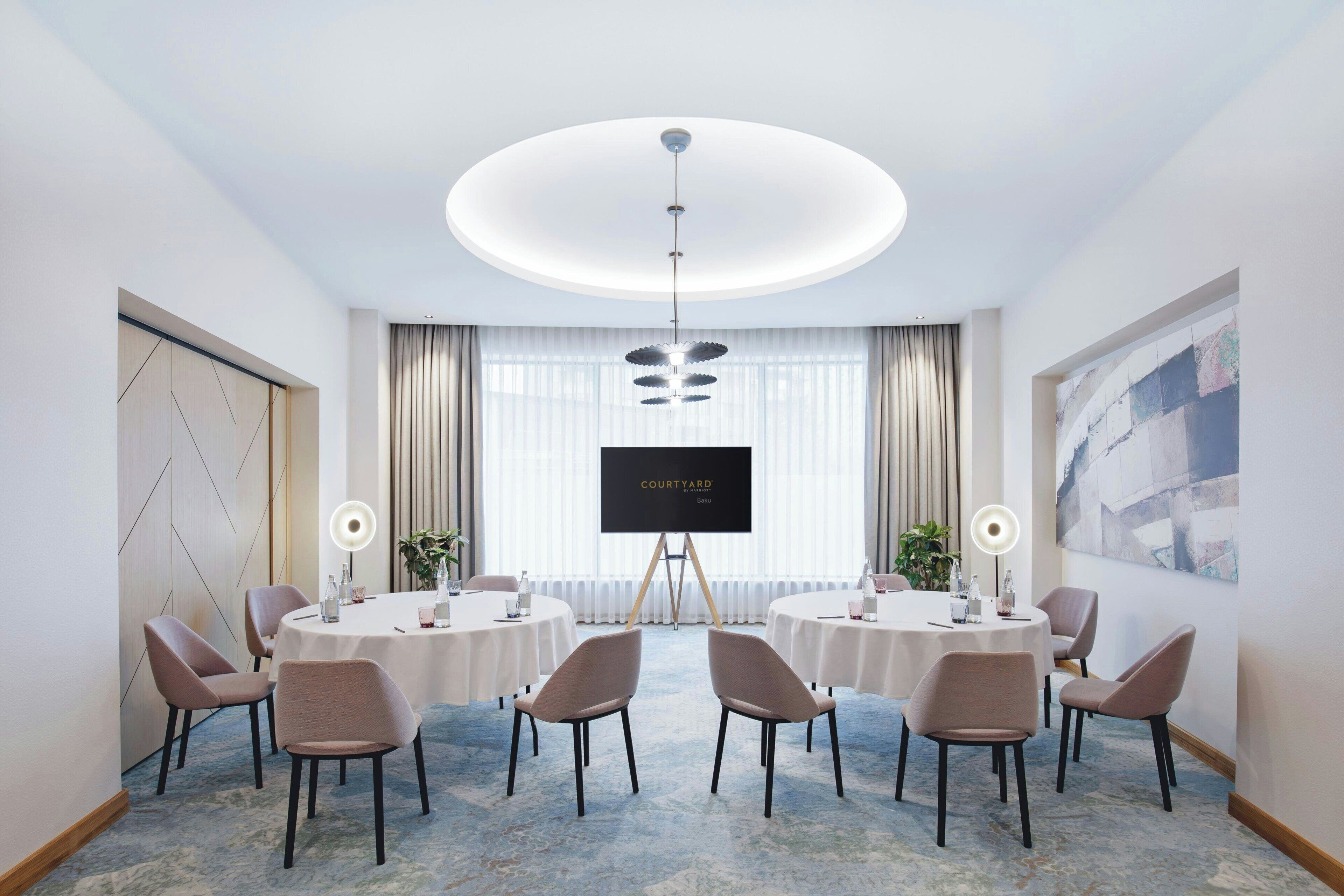 Ett konferensrum med en stor skärm som visar texten ”COURTYARD”, runda bord, stolar och en modern taklampa.