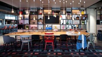 A modern bar area with a long wooden table, multiple chairs, hanging pendant lights, and a variety of decorative items on shelves.
