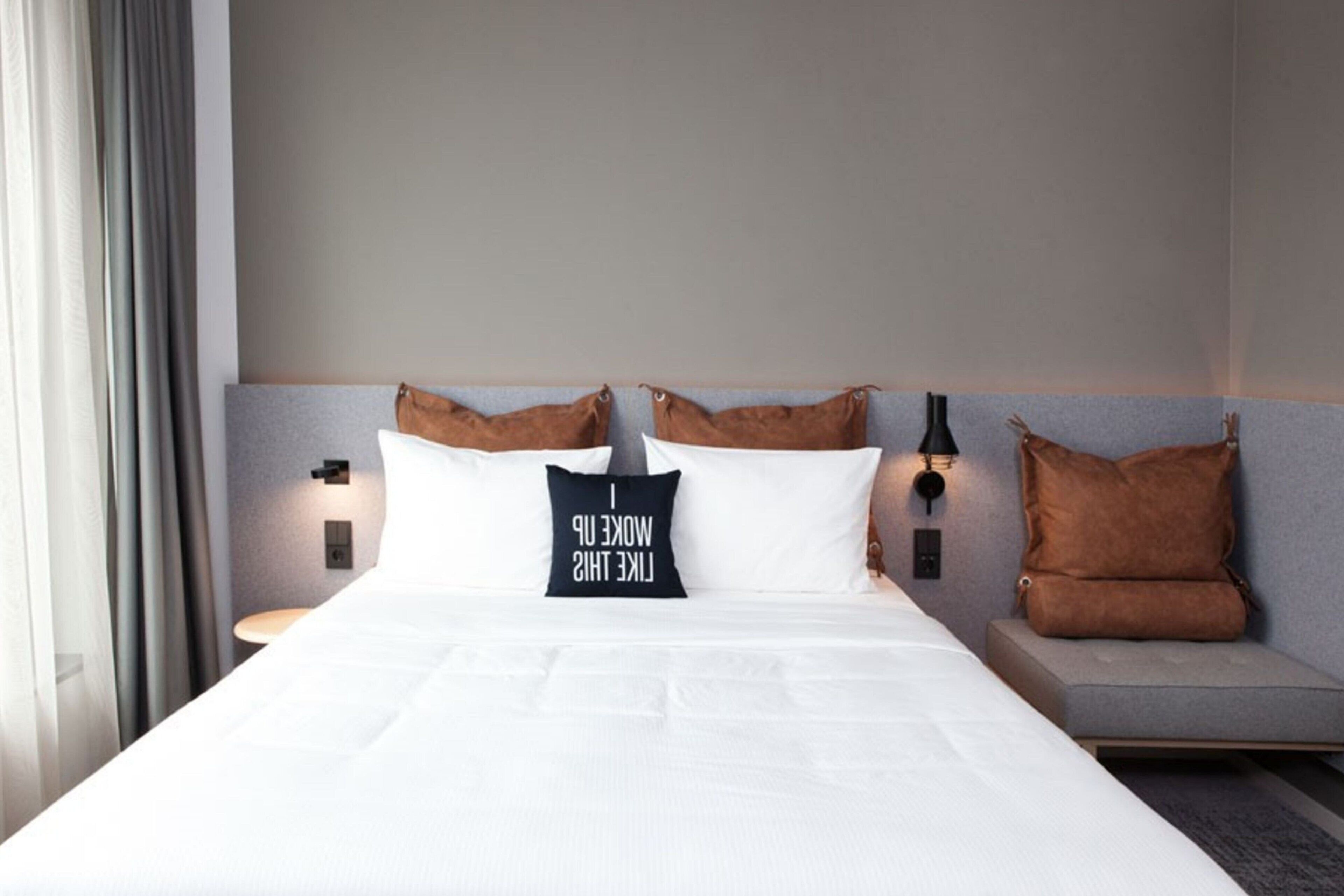 A neatly made bed with white linens, two pillows, and a bedside table with a lamp.