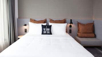 Una cama bien hecha con sábanas blancas, dos almohadas y una mesita de noche con lámpara.