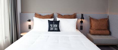 A neatly made bed with white linens, two pillows, and a bedside table with a lamp.