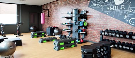 Un gimnasio con equipos de ejercicio variados, incluyendo mancuernas, kettlebells y un saco de boxeo.