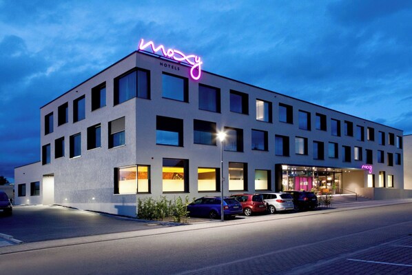A modern hotel with a neon sign, multiple parking spaces, and a well-lit entrance.