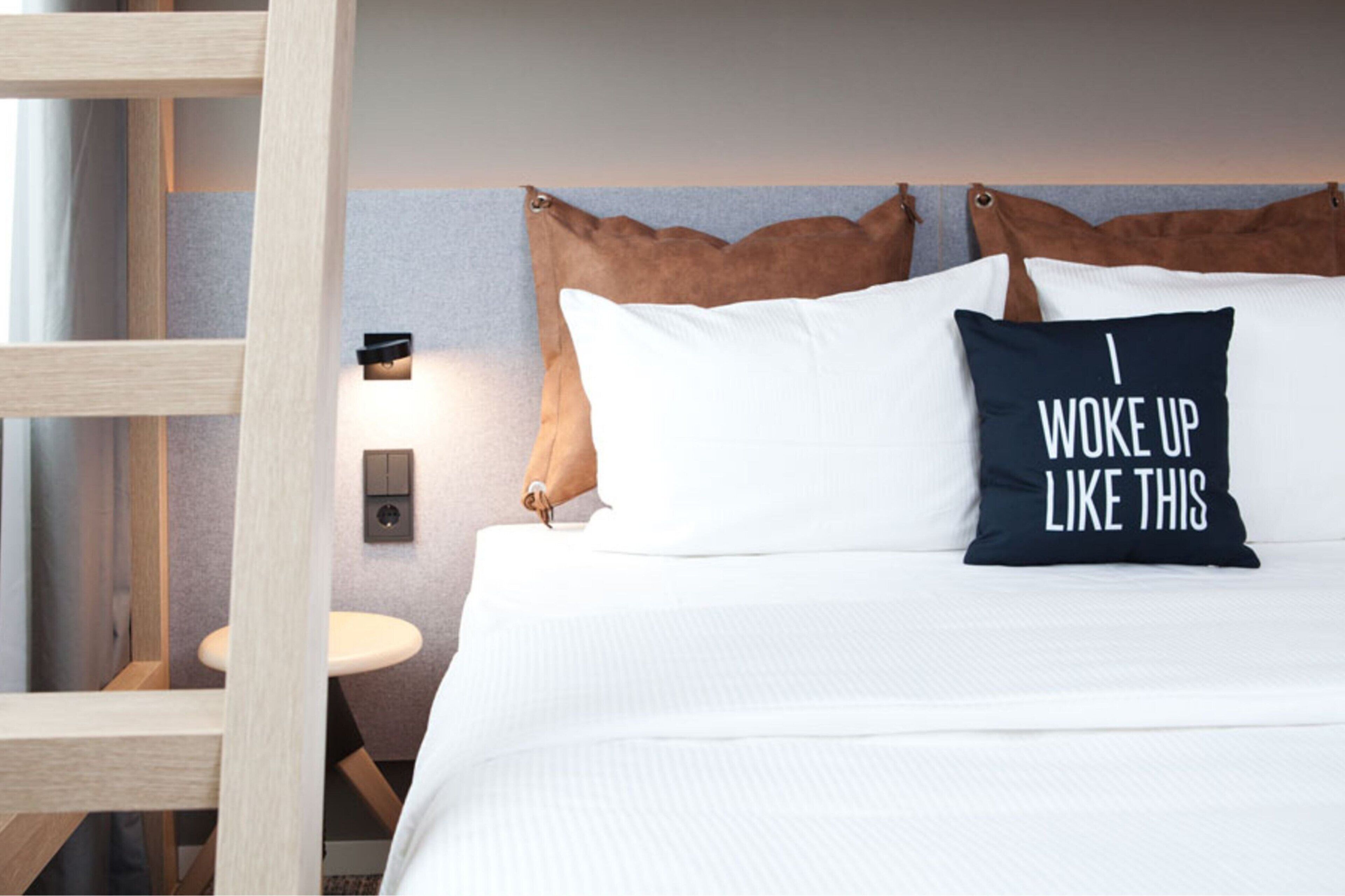 A neatly made bed with white bedding and two pillows, one with a motivational quote.