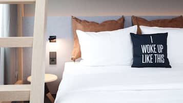 A neatly made bed with white bedding and two pillows, one with a motivational quote.