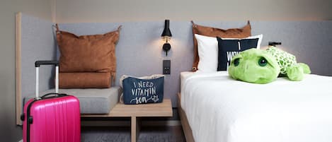 Ein Hotelzimmer mit Bett, einem Kissen mit Schriftzug, einem Koffer und einem Stofftier.