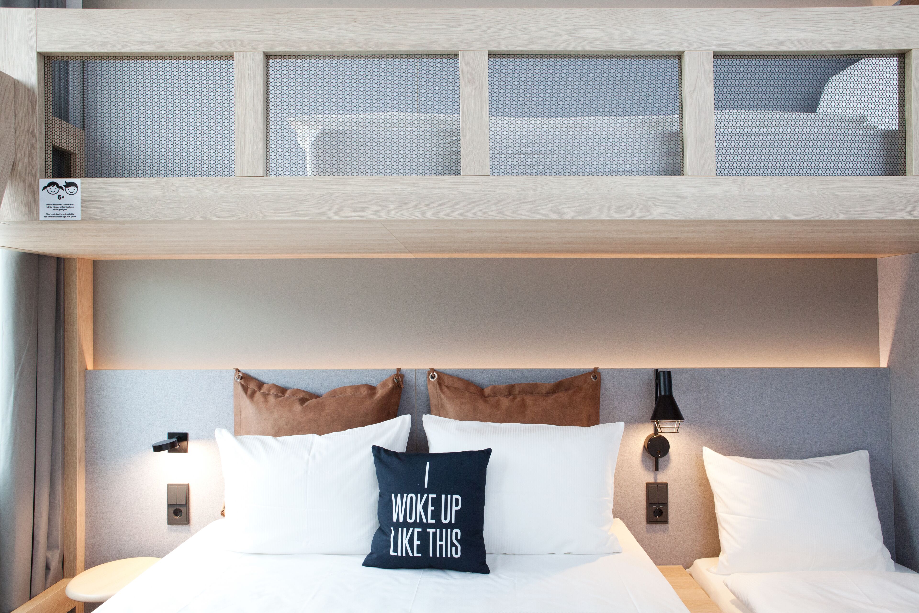 A hotel room with a bunk bed, a headboard with a light fixture, and a pillow with a motivational quote.