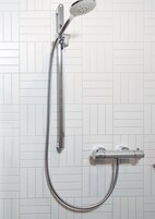 A shower with a handheld showerhead and a wall-mounted control valve.