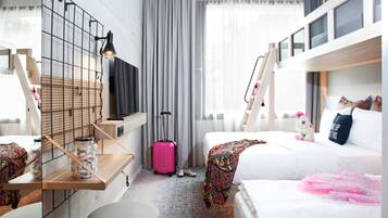 A hotel room with a bunk bed, a desk with a lamp, a suitcase, and a plush toy on the bed.