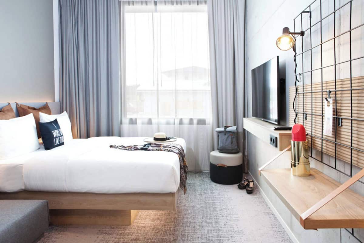 Une chambre d’hôtel moderne avec un grand lit, une télévision, une table de chevet en bois et une vue par la fenêtre.