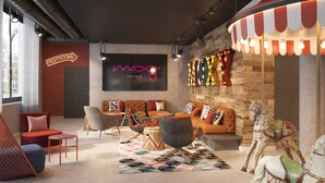 Un moderno vestíbulo de hotel con un letrero grande para los baños, un área de estar con sofás y sillones, y una decoración con un caballo de carrusel.